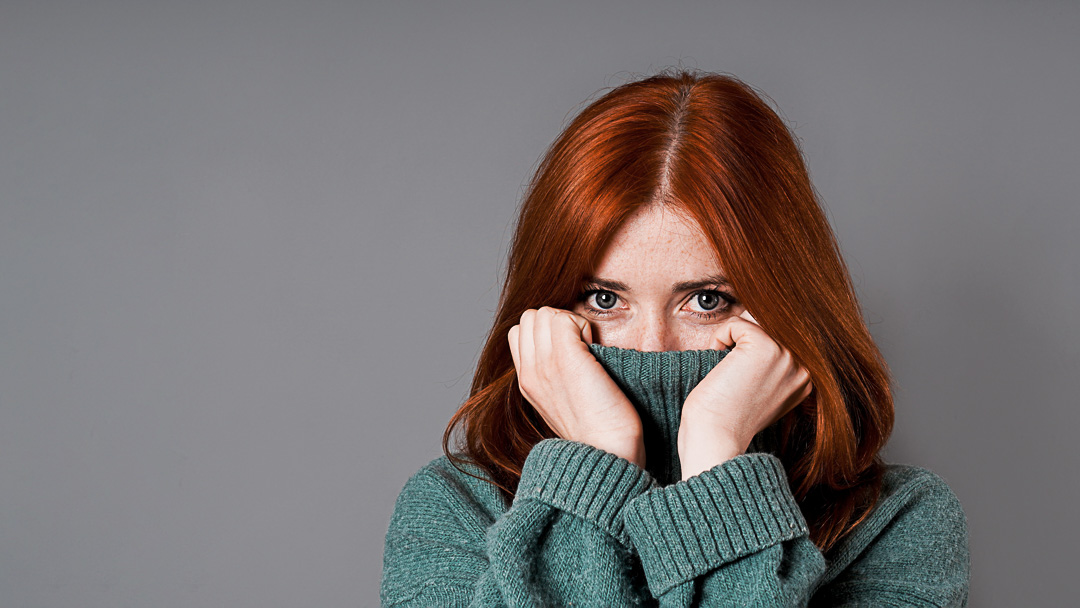 shy or embarrassed woman pulling turtleneck sweater over her face