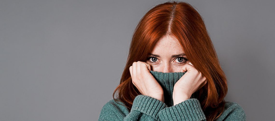 shy or embarrassed woman pulling turtleneck sweater over her face